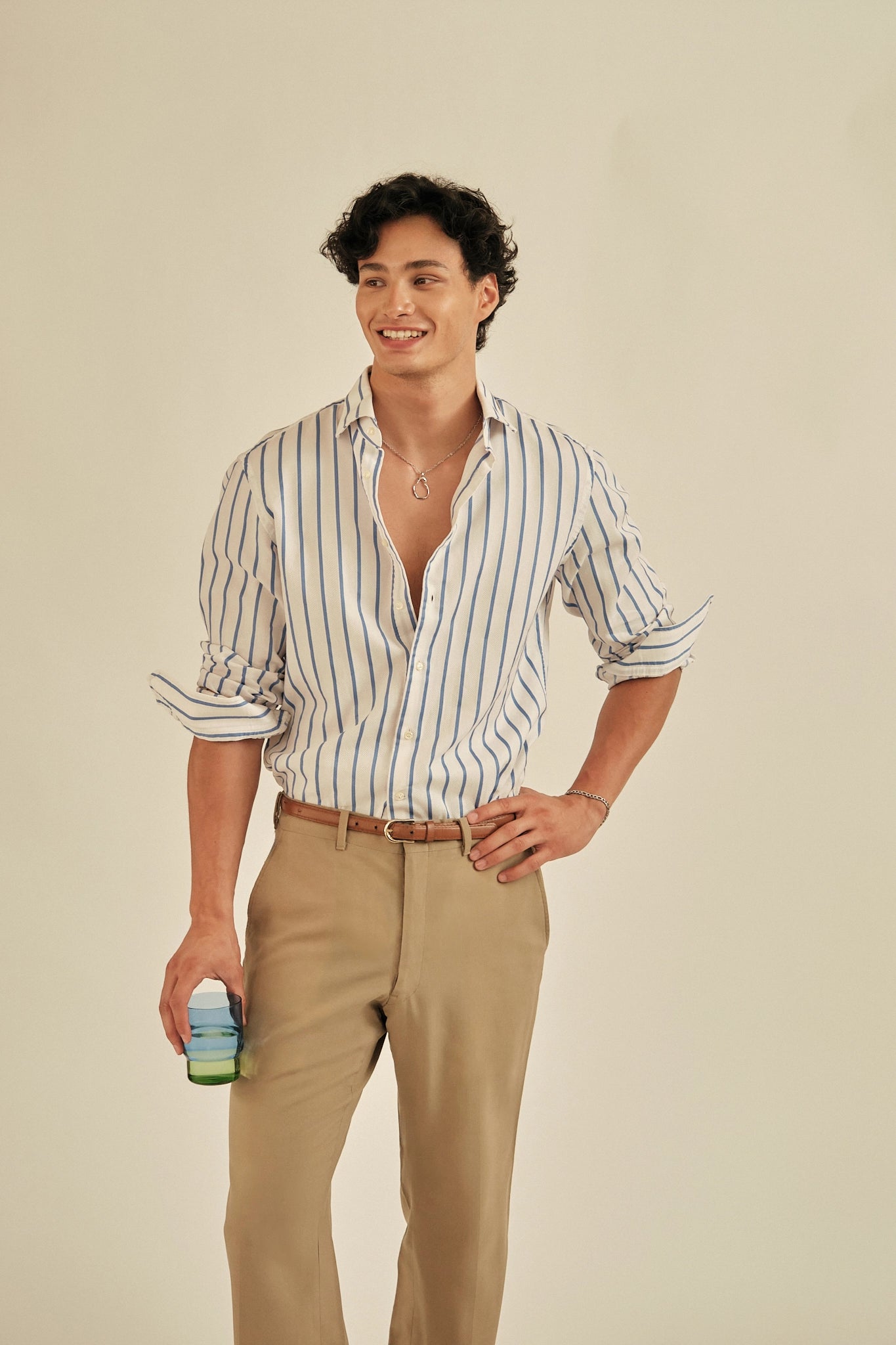 Man wearing a striped shirt and beige pants holding a bottle against a plain background
