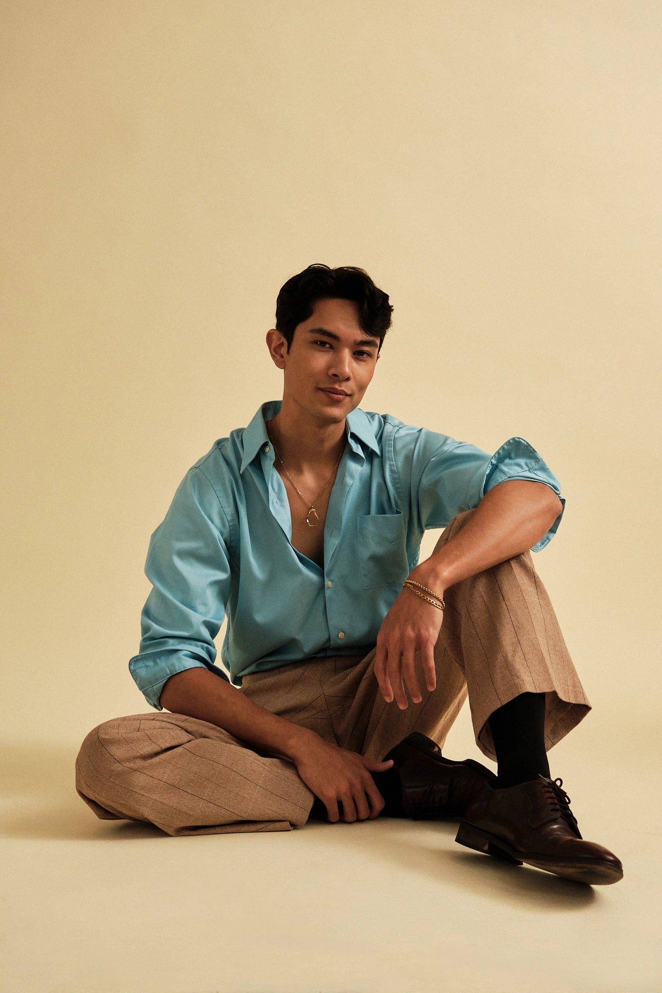 Man sitting on a beige floor wearing a light blue shirt and beige pants.