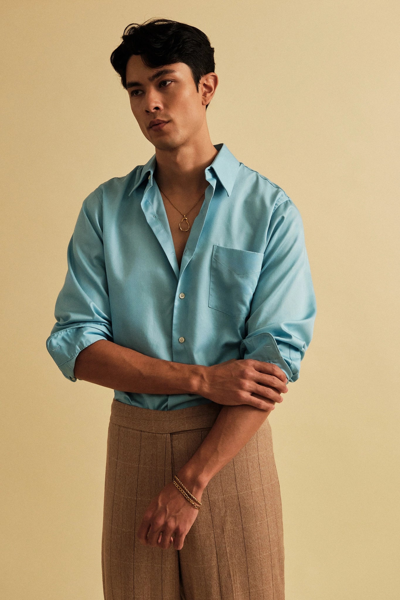 Man wearing a light blue shirt and brown pants against a beige background