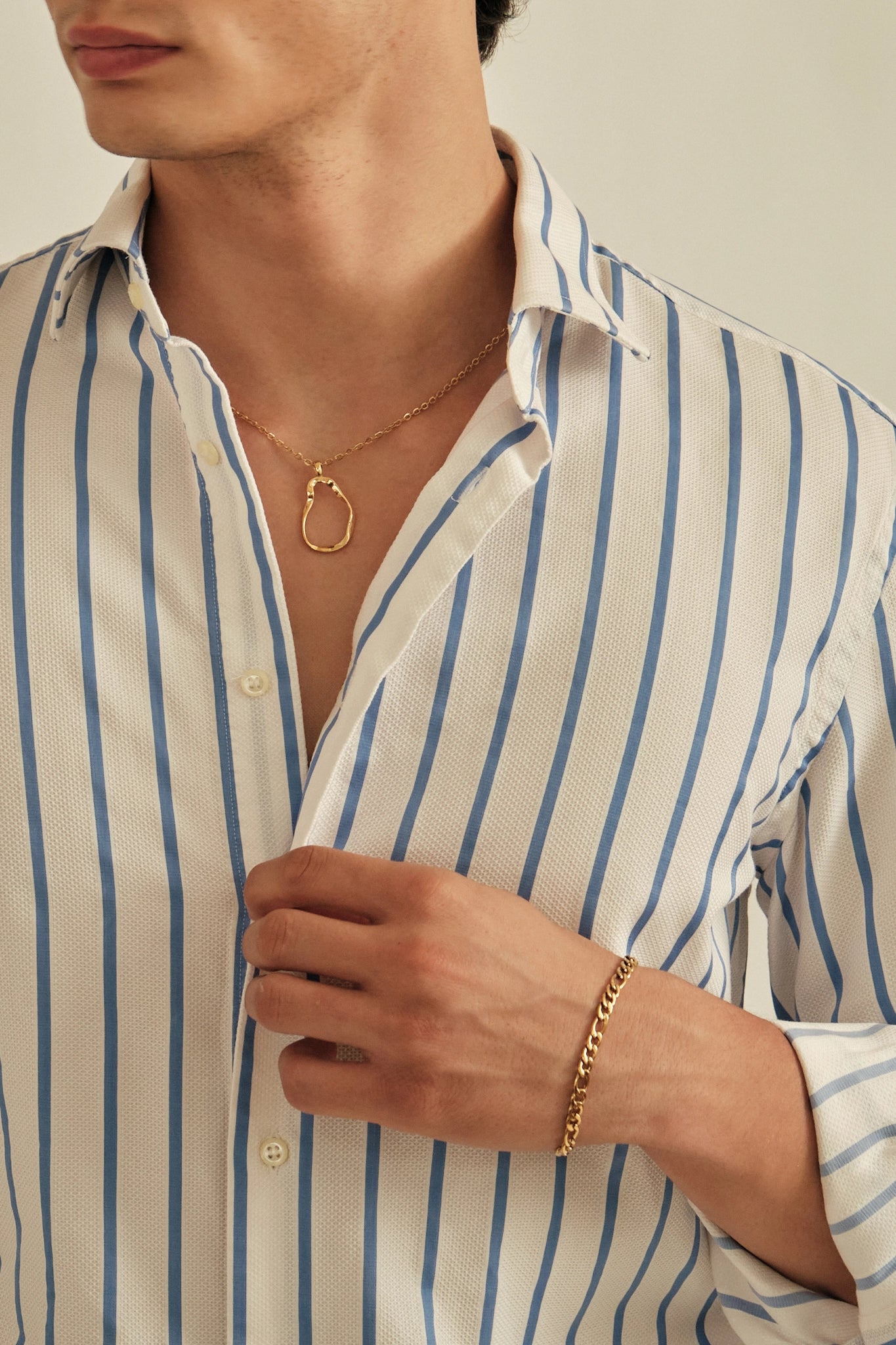 Person wearing a gold necklace and bracelet with a striped shirt