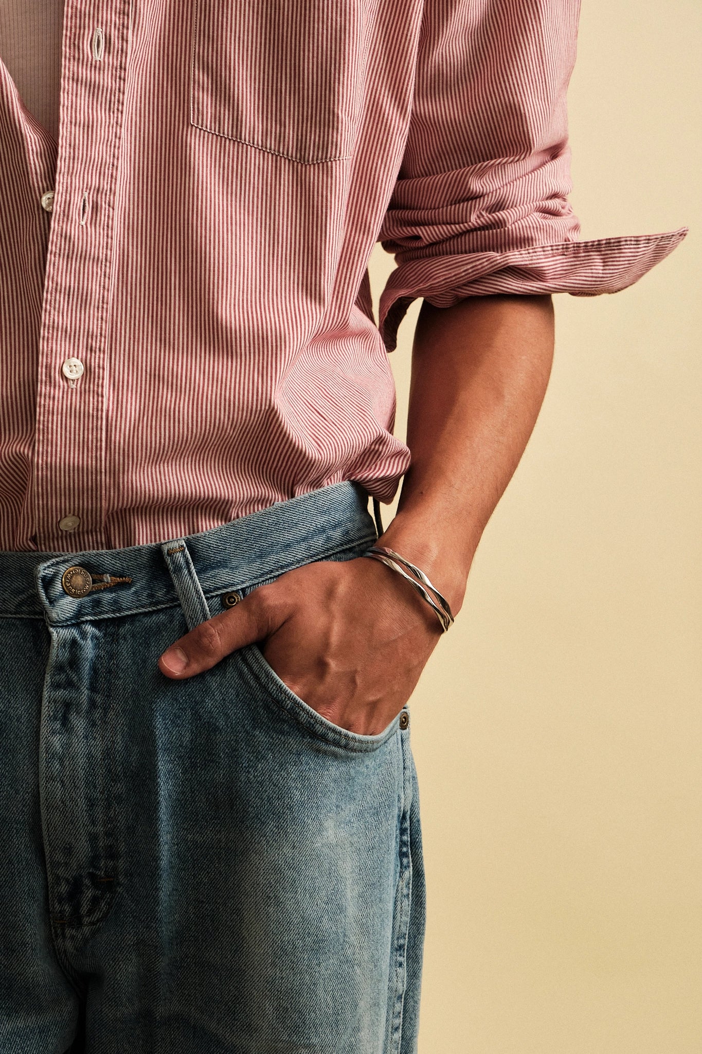 Person wearing a pink striped shirt and blue jeans against a beige background