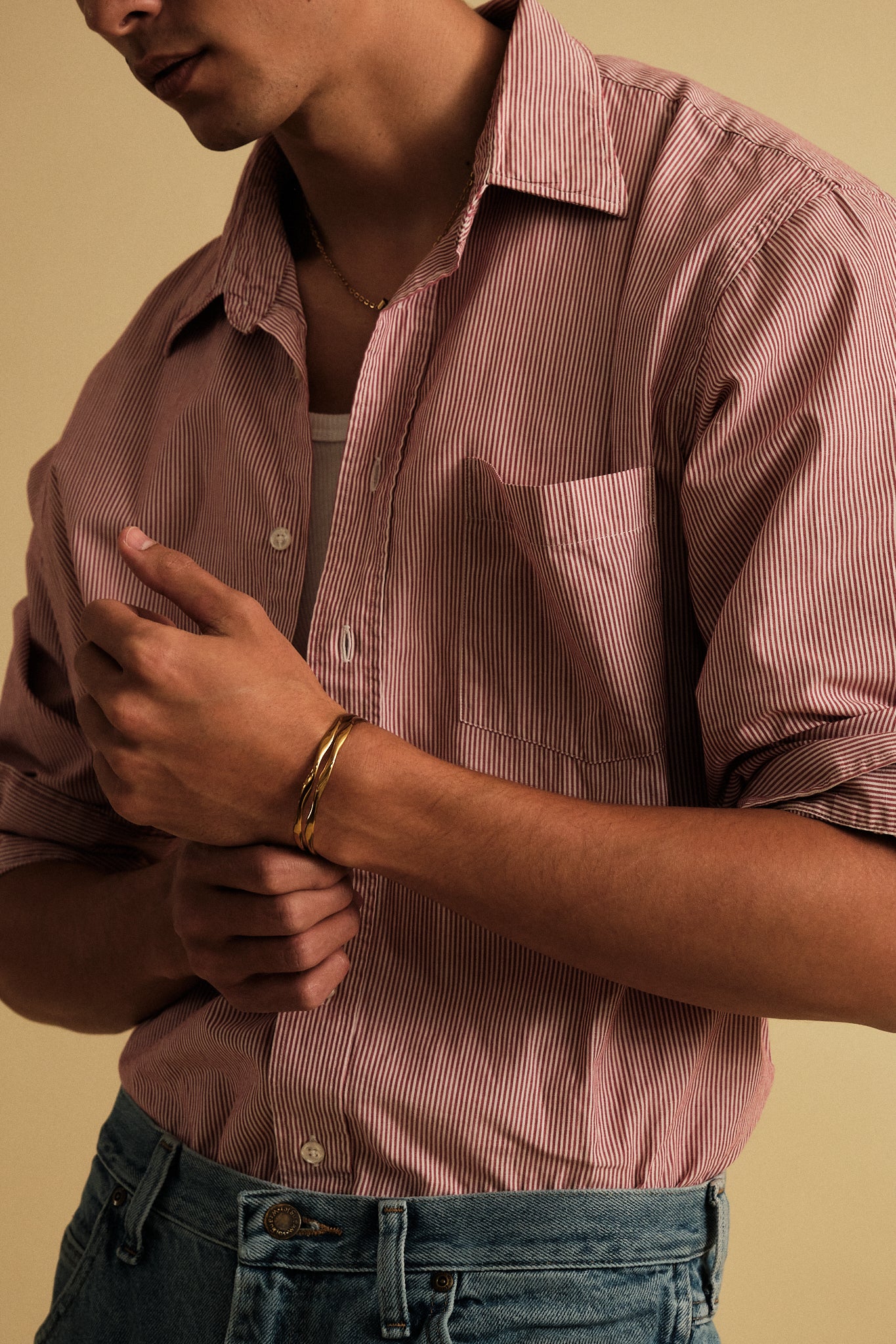 Man wearing a pink striped shirt and blue jeans against a beige background