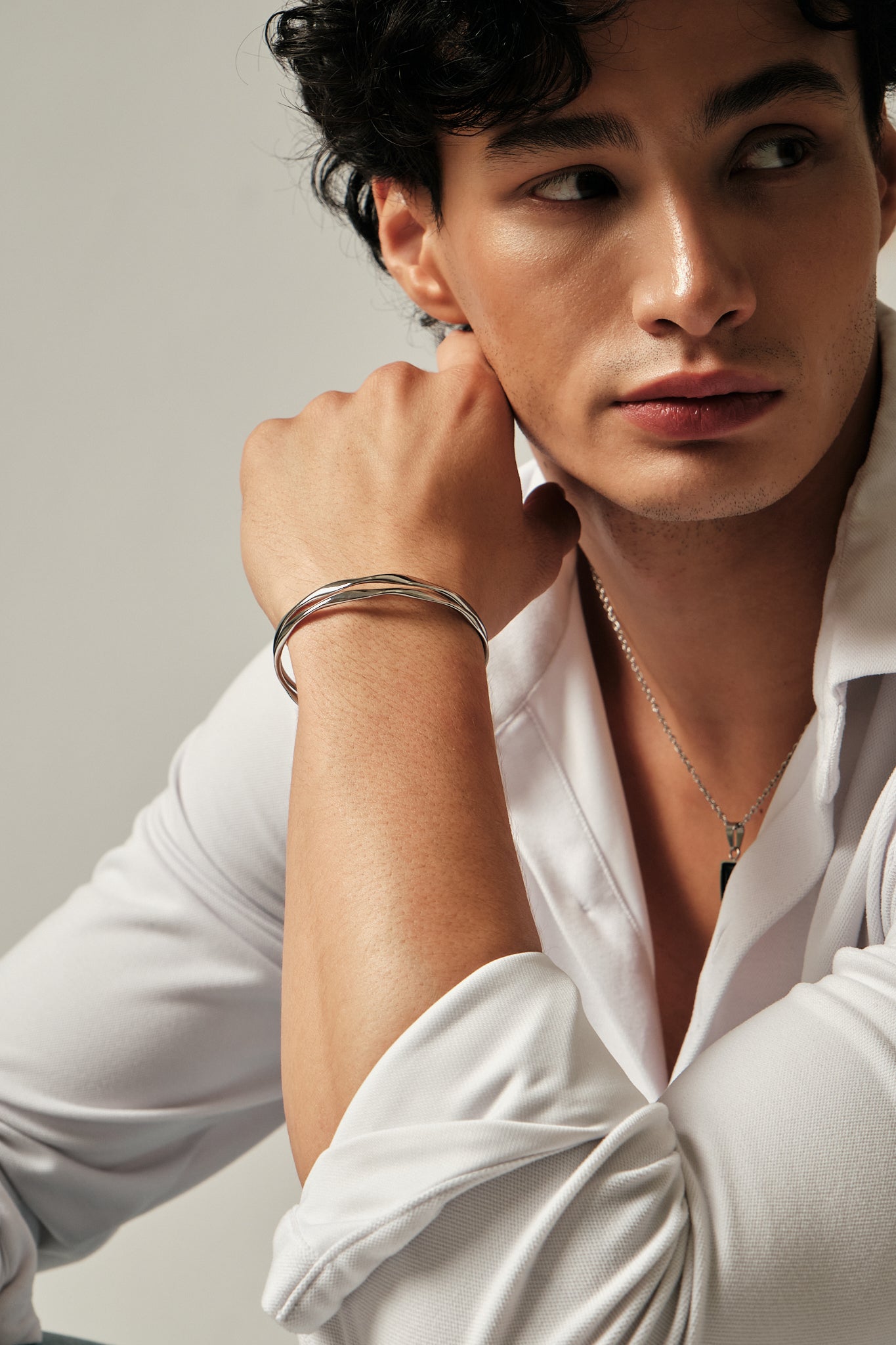 Person wearing a white shirt with jewelry on a neutral background