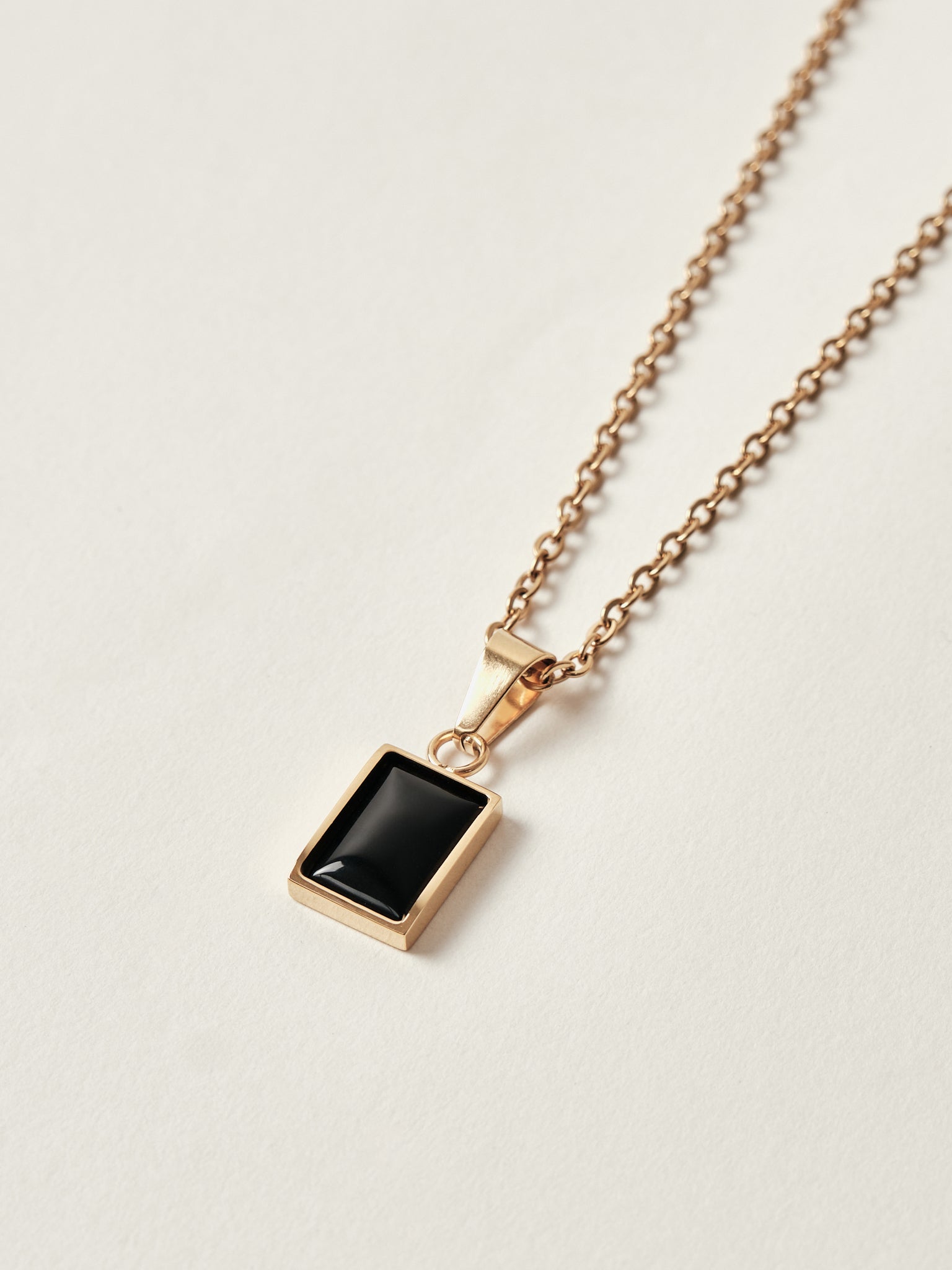 Rose gold necklace with a black square pendant on a light gray background