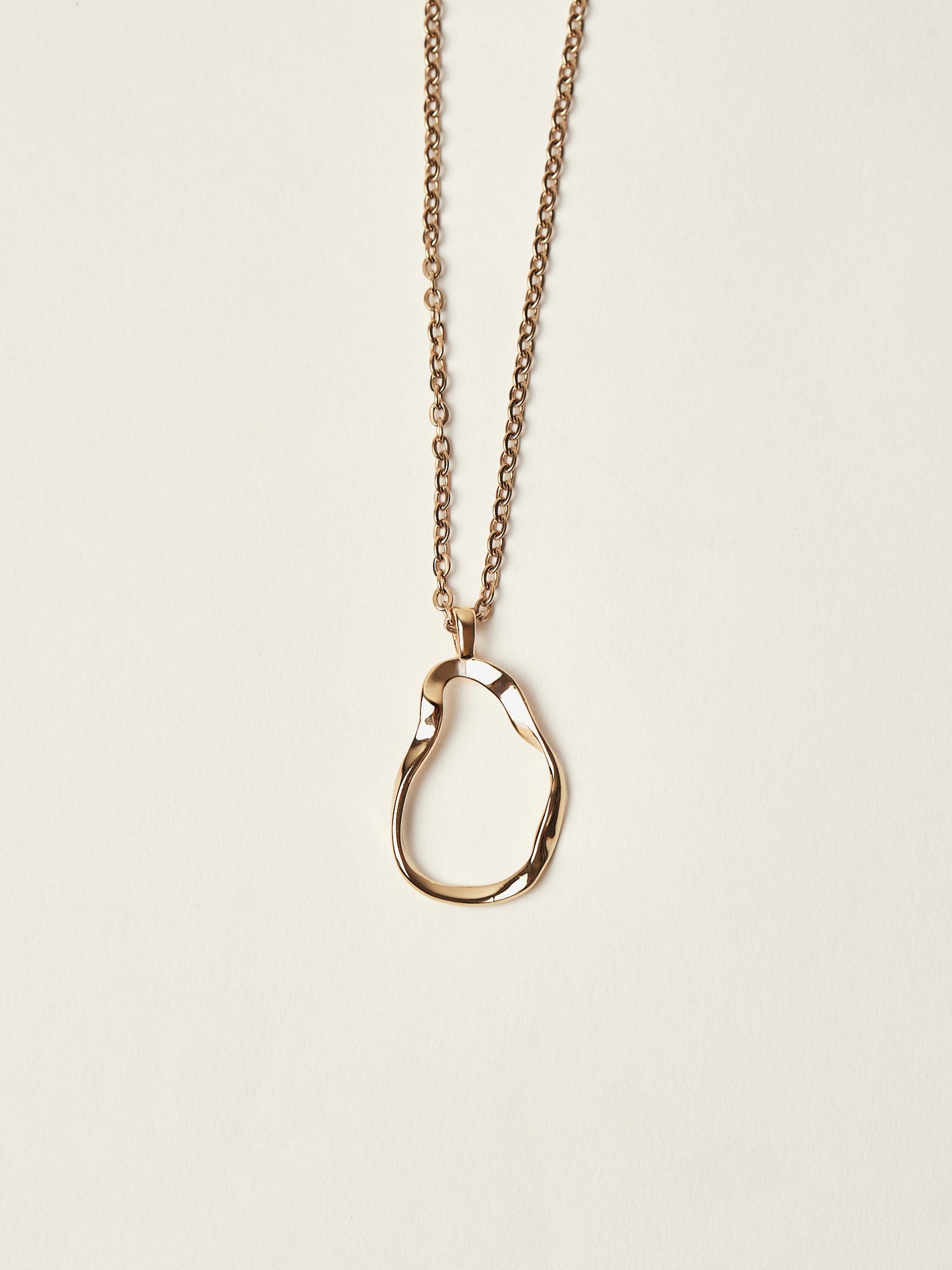 Gold necklace with a unique pendant on a beige background