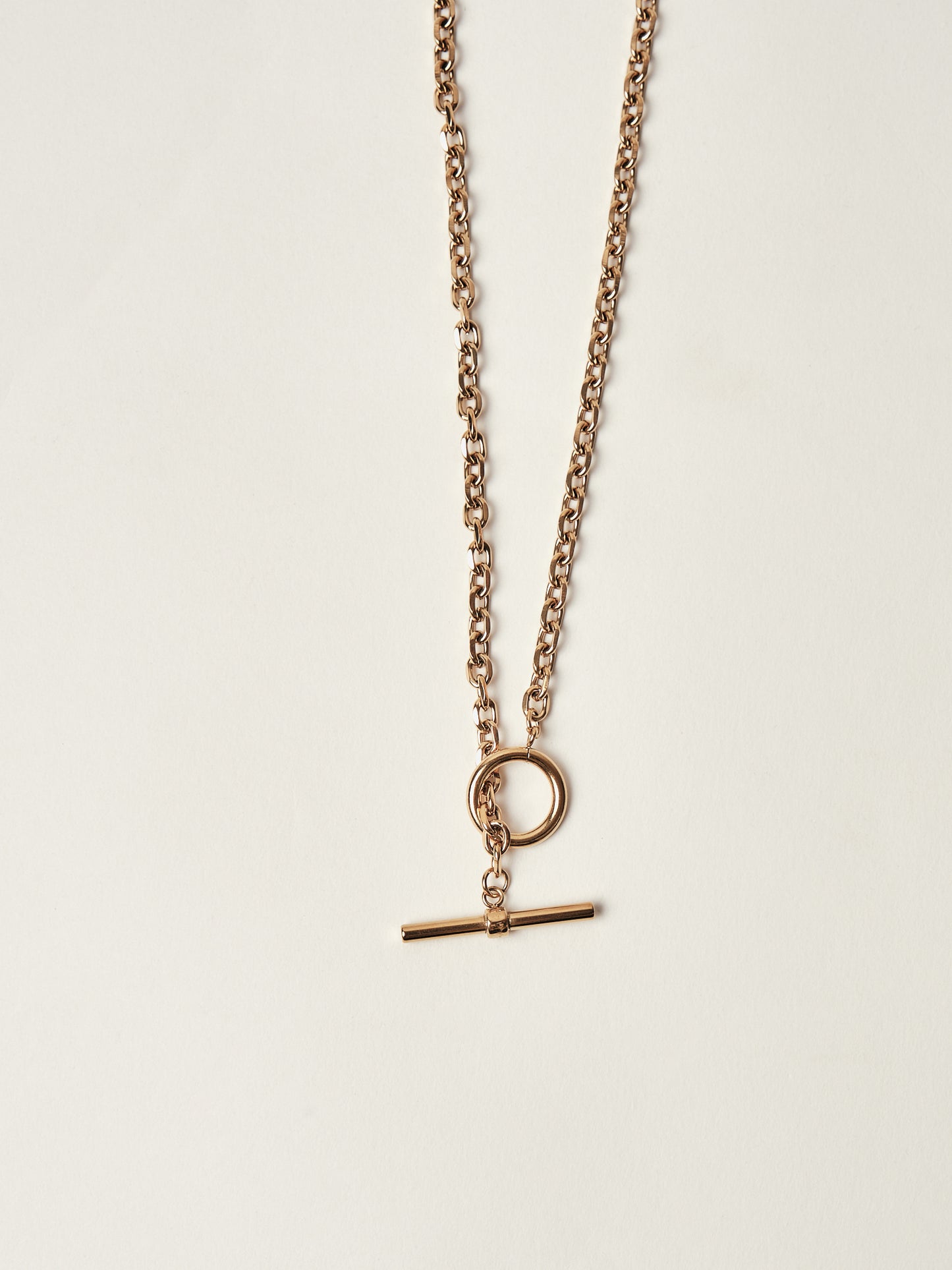Gold necklace with a round pendant and a bar-shaped charm on a light beige background