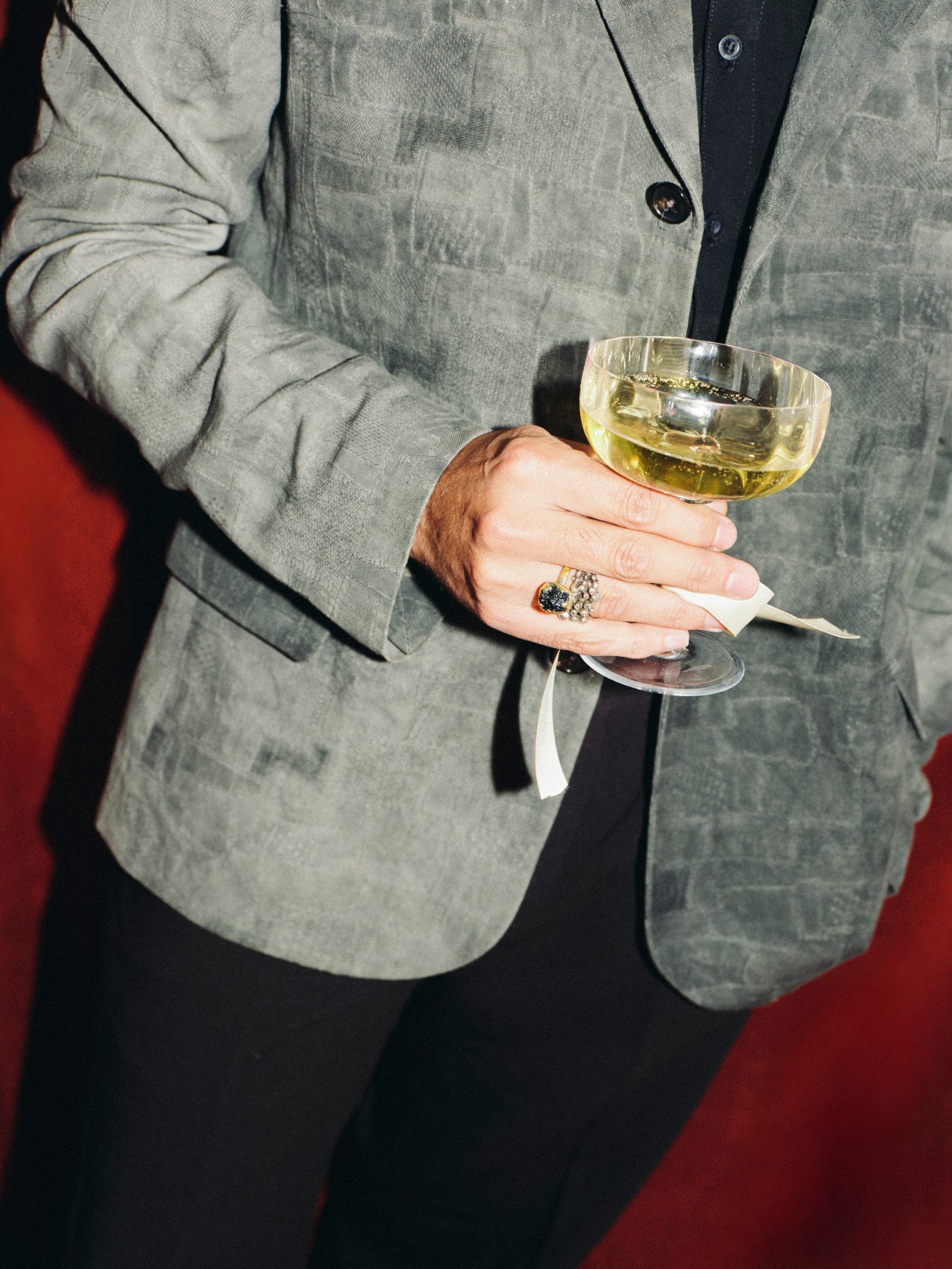 Person holding a glass of white wine with a gray blazer and red background
