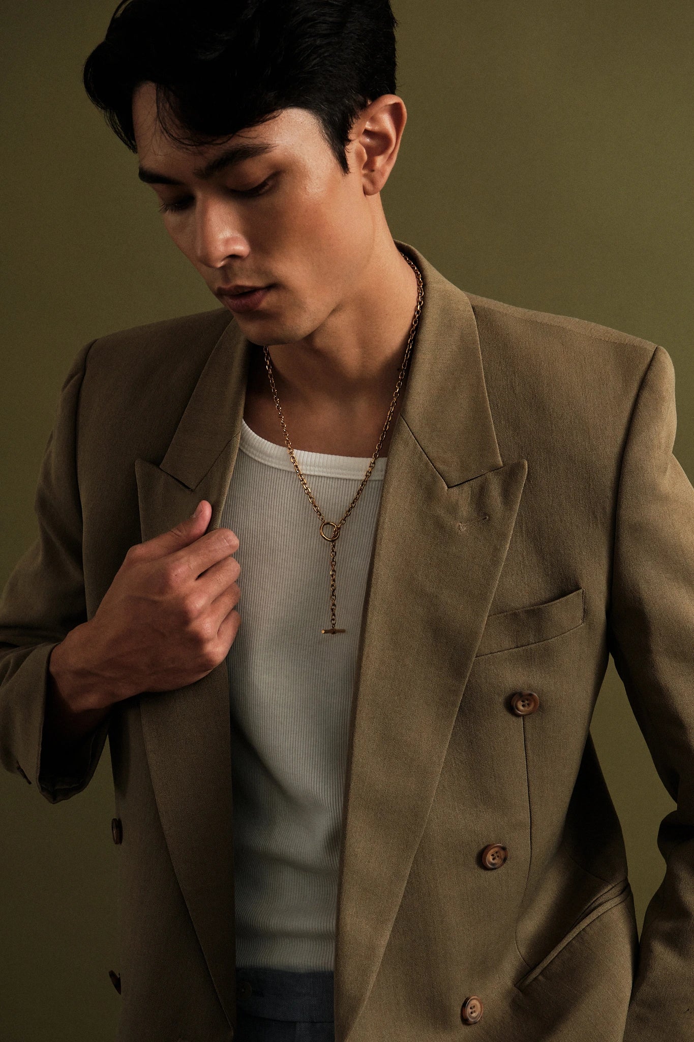 Man wearing a brown blazer over a white shirt against a green background