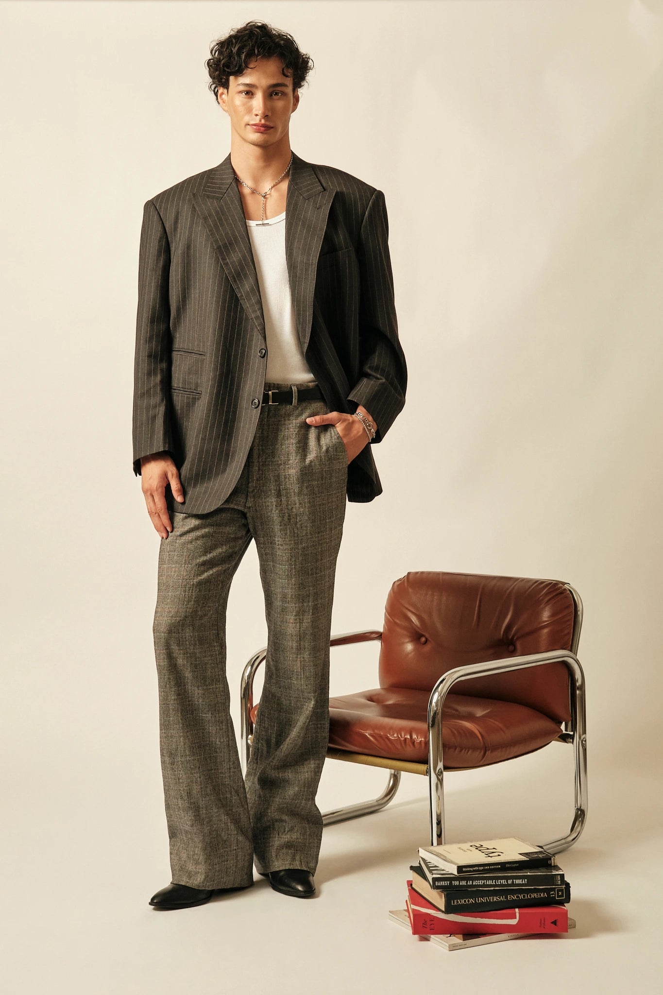Man in a gray suit standing next to a brown leather chair with books on a white background