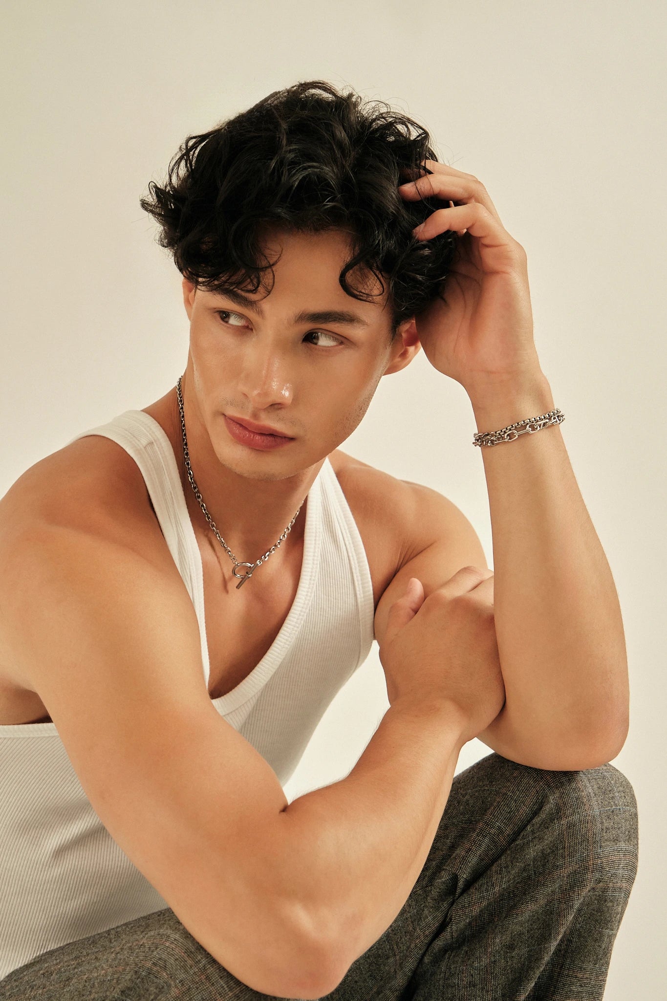 Man wearing a white tank top and gray pants against a plain background