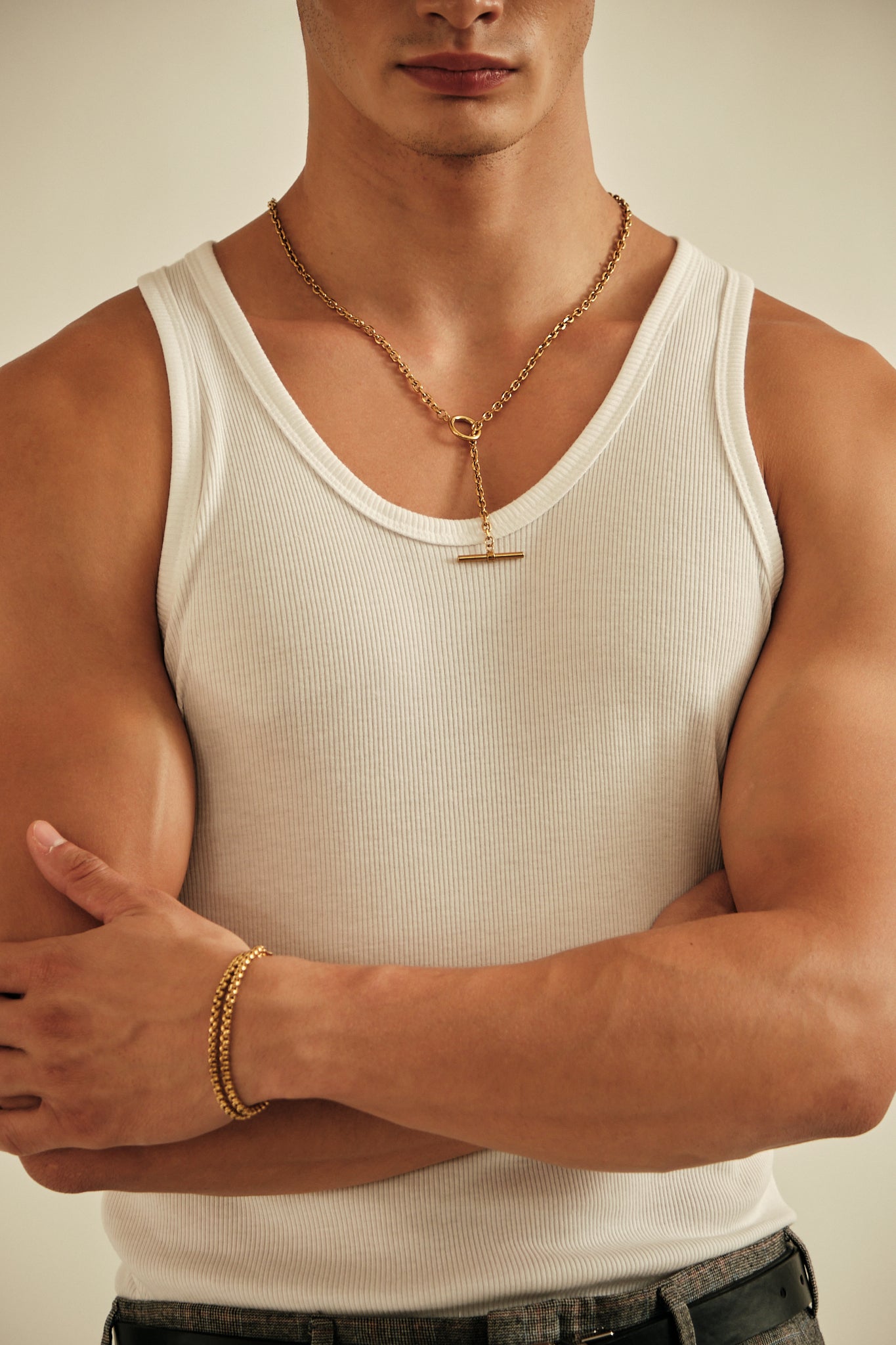 Man wearing a white tank top and gold jewelry against a neutral background