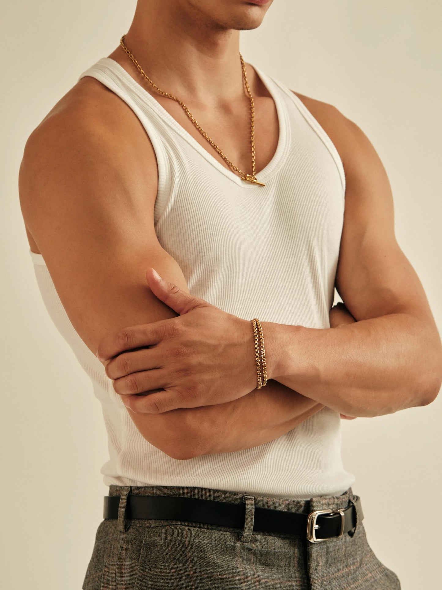 Person wearing a white tank top and gray pants with a neutral background