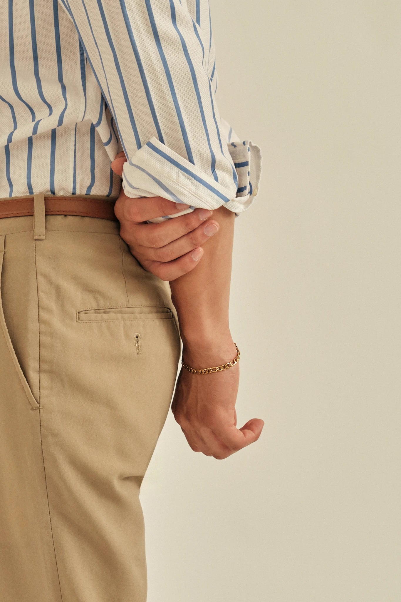 Person wearing a striped shirt and beige pants with a plain background
