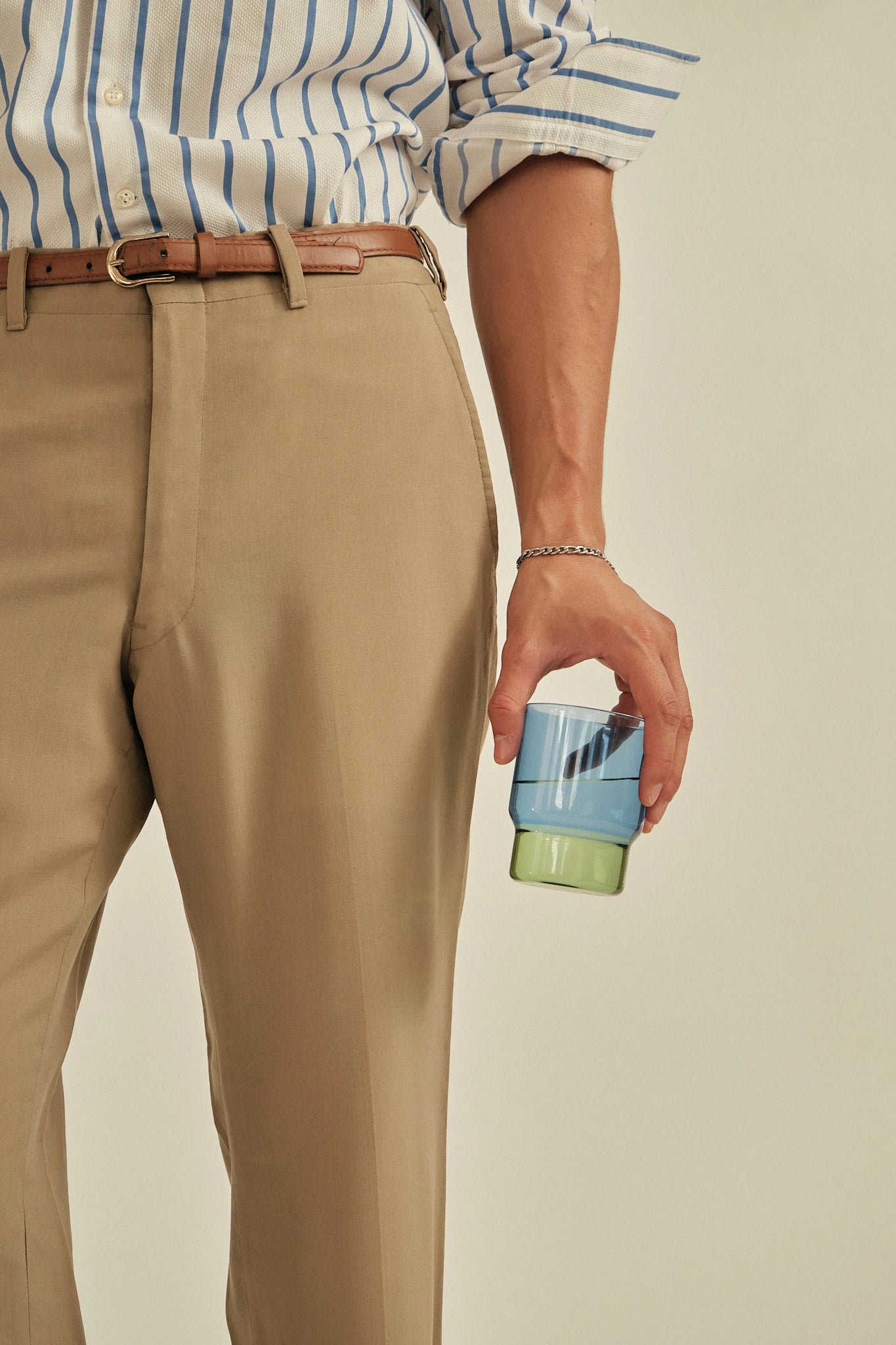 Person wearing beige pants and a striped shirt, holding a blue and green container.
