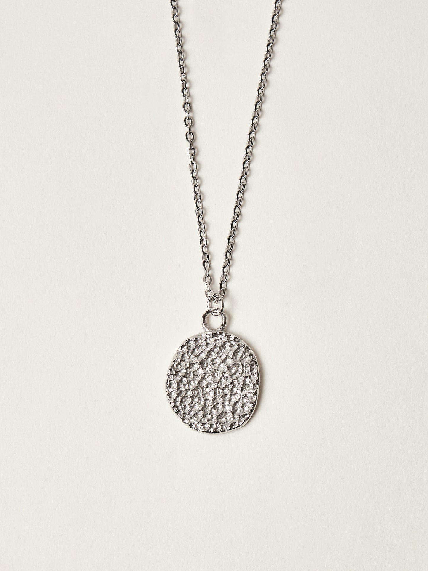 Silver necklace with a textured round pendant on a light gray background