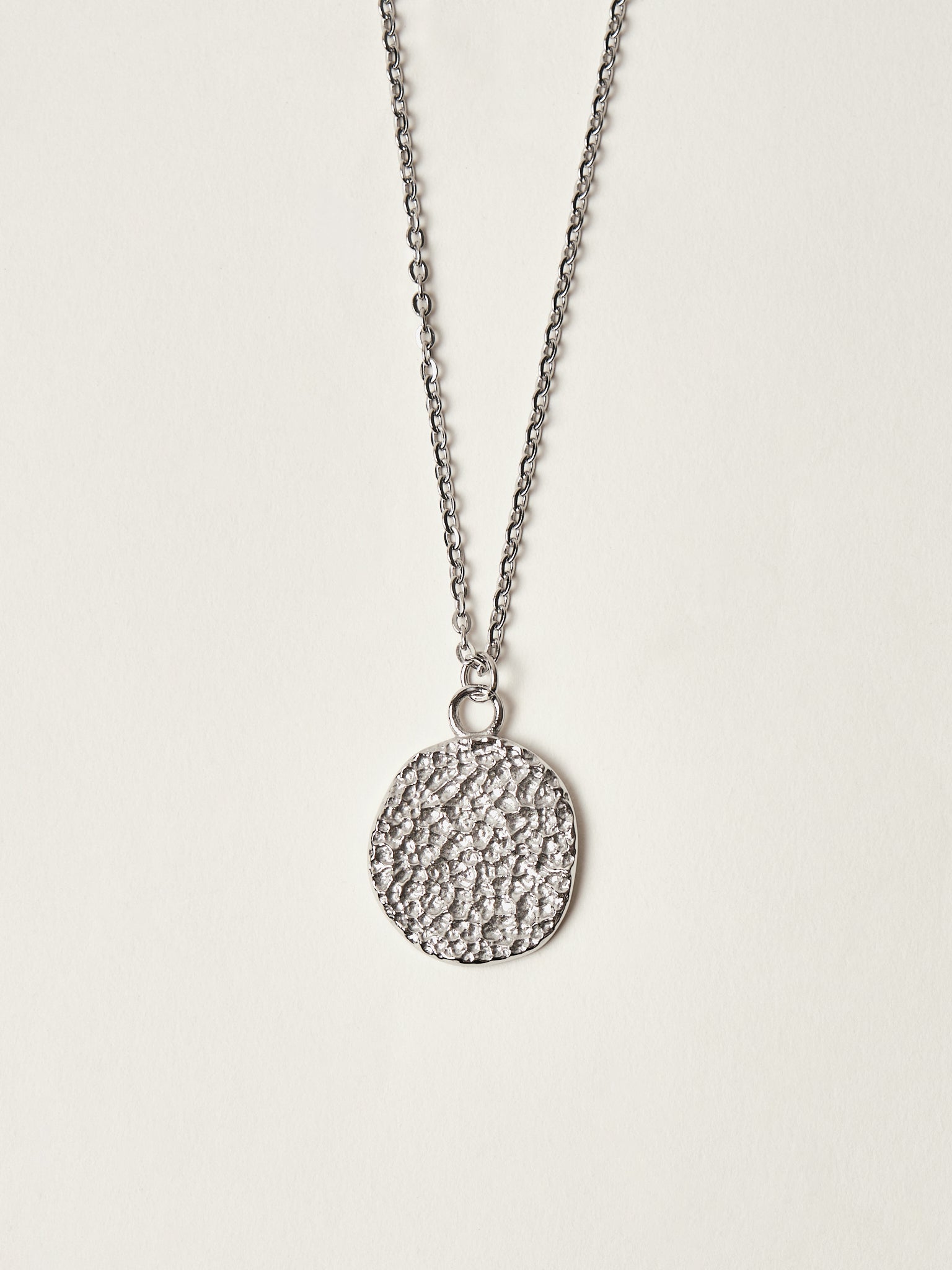 Silver necklace with a textured round pendant on a light gray background