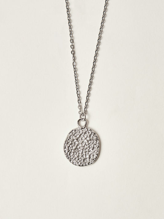 Silver necklace with a textured round pendant on a light gray background
