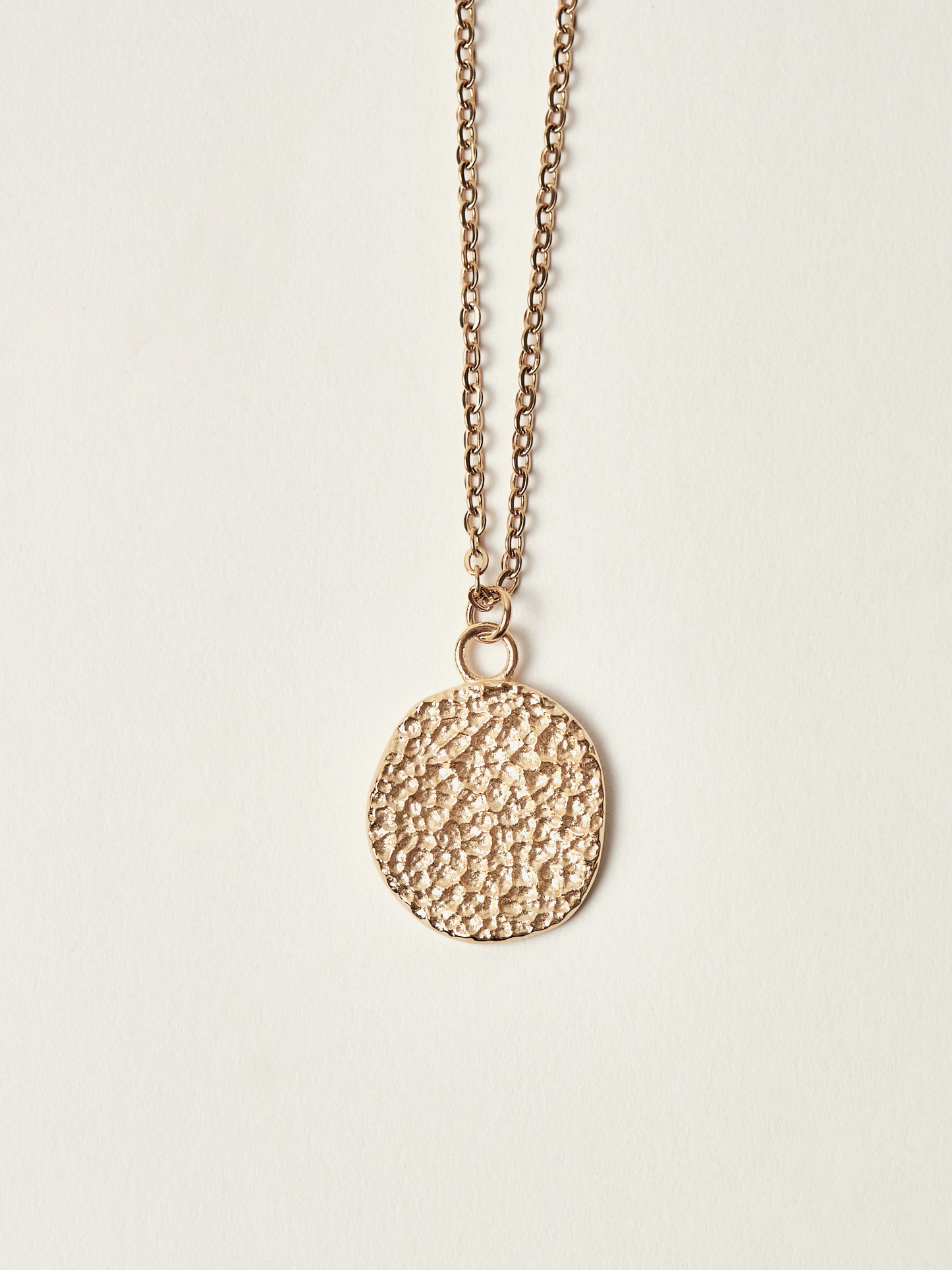 Gold necklace with a textured pendant on a light beige background