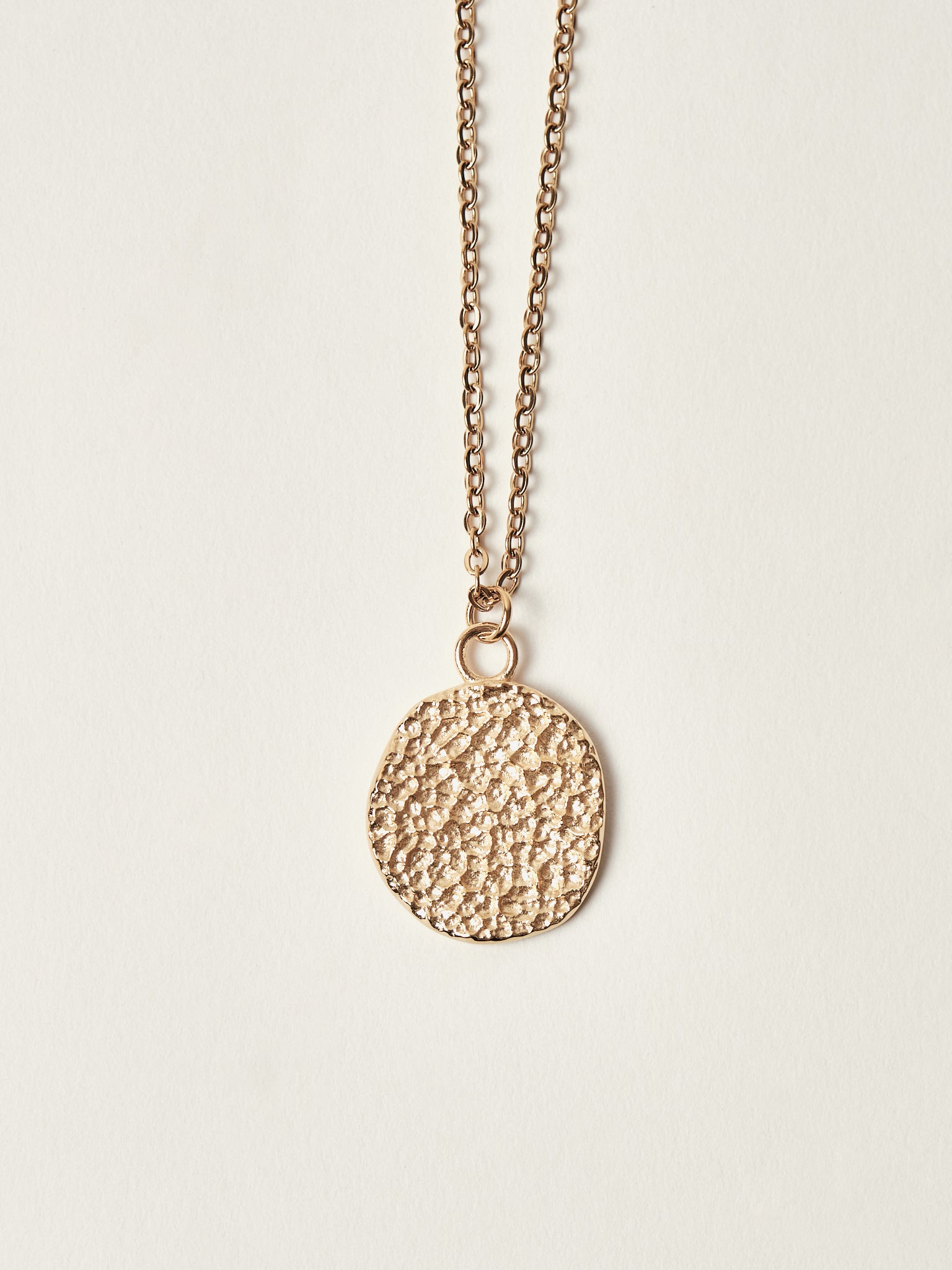 Gold necklace with a textured pendant on a light beige background
