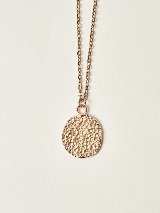 Gold necklace with a textured pendant on a light beige background