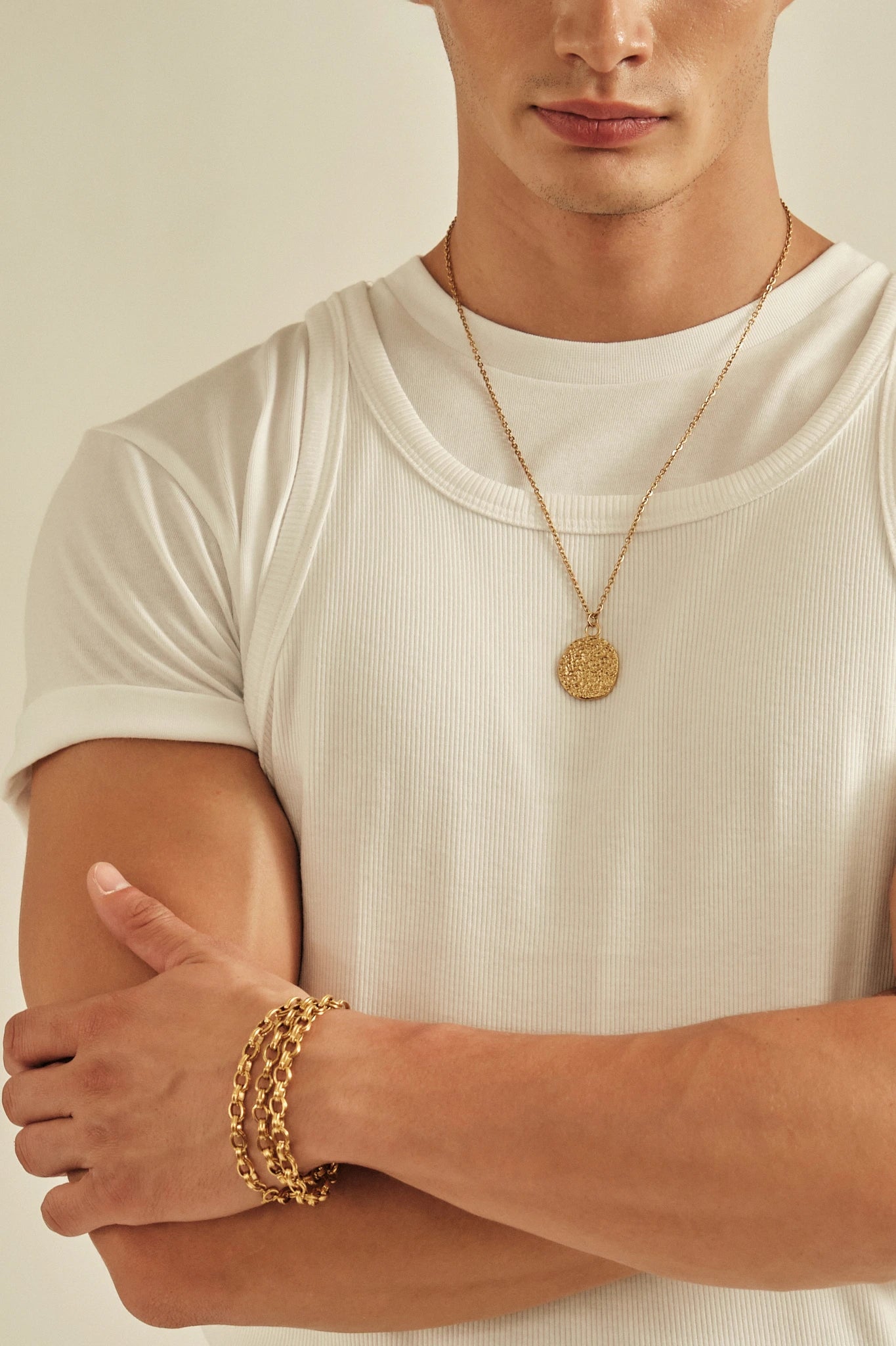 Man wearing a gold necklace and bracelet on a plain background