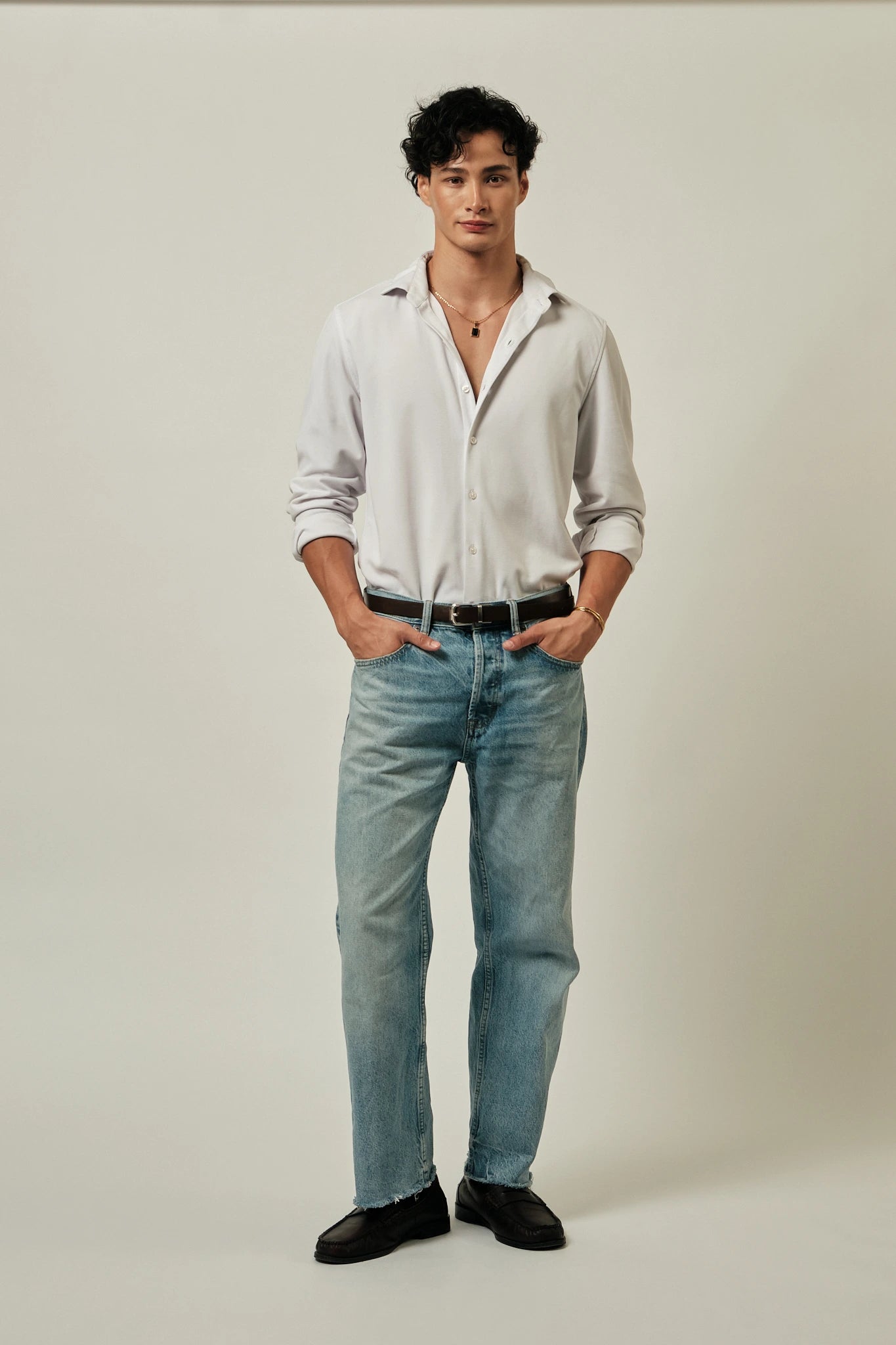 Man wearing a white shirt, blue jeans, and black shoes against a plain background
