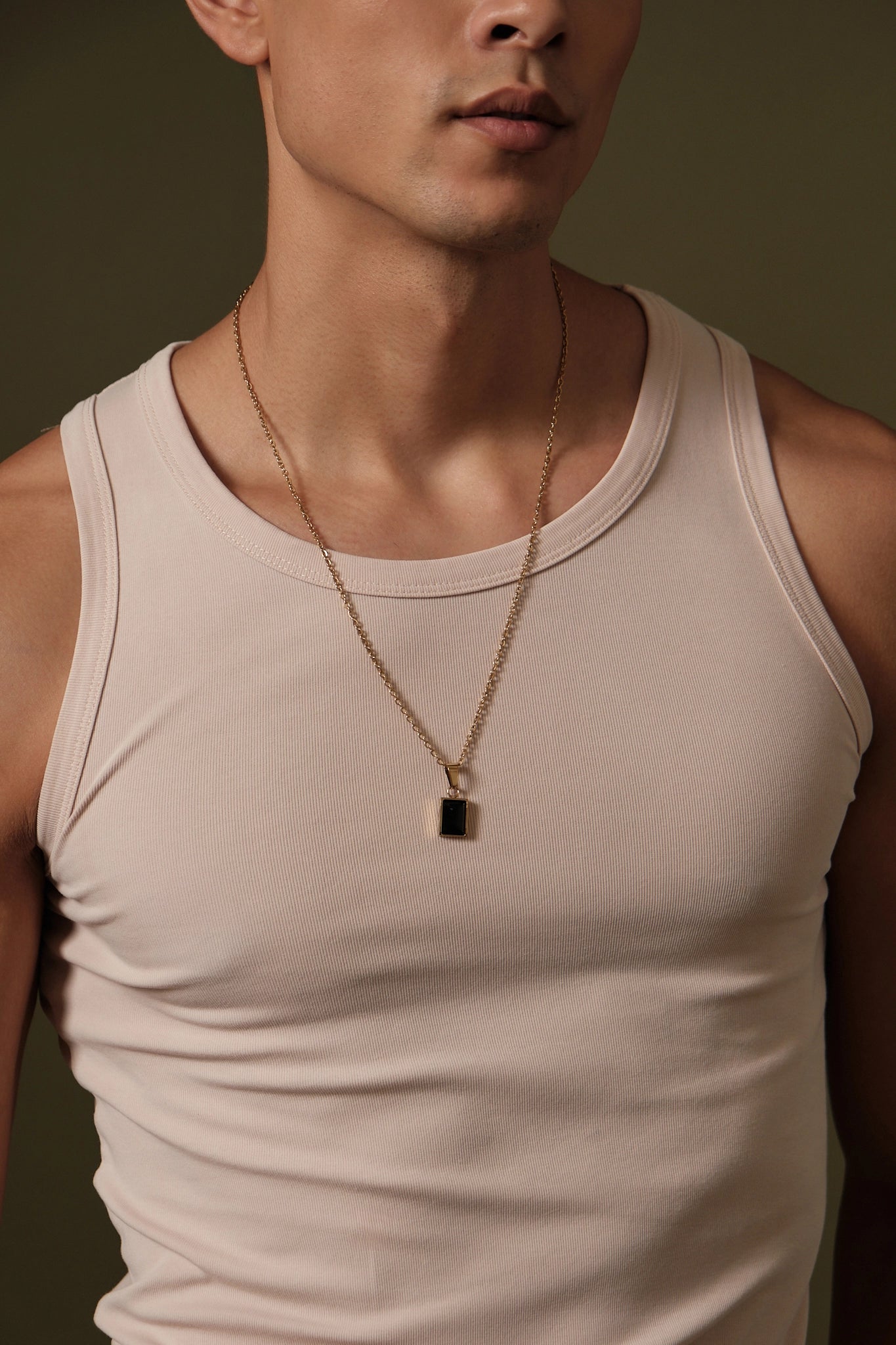 Man wearing a beige tank top and gold necklace against a brown background
