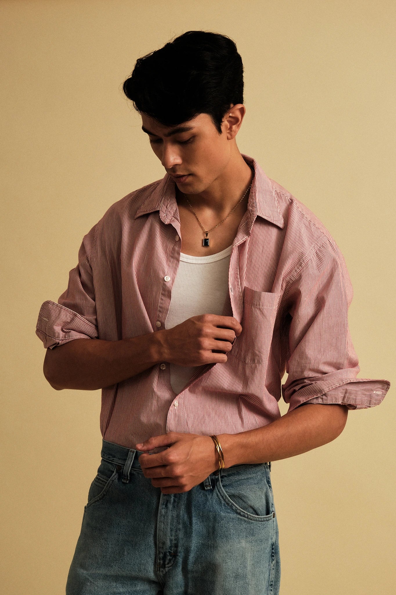 Man wearing a pink shirt and blue jeans against a beige background
