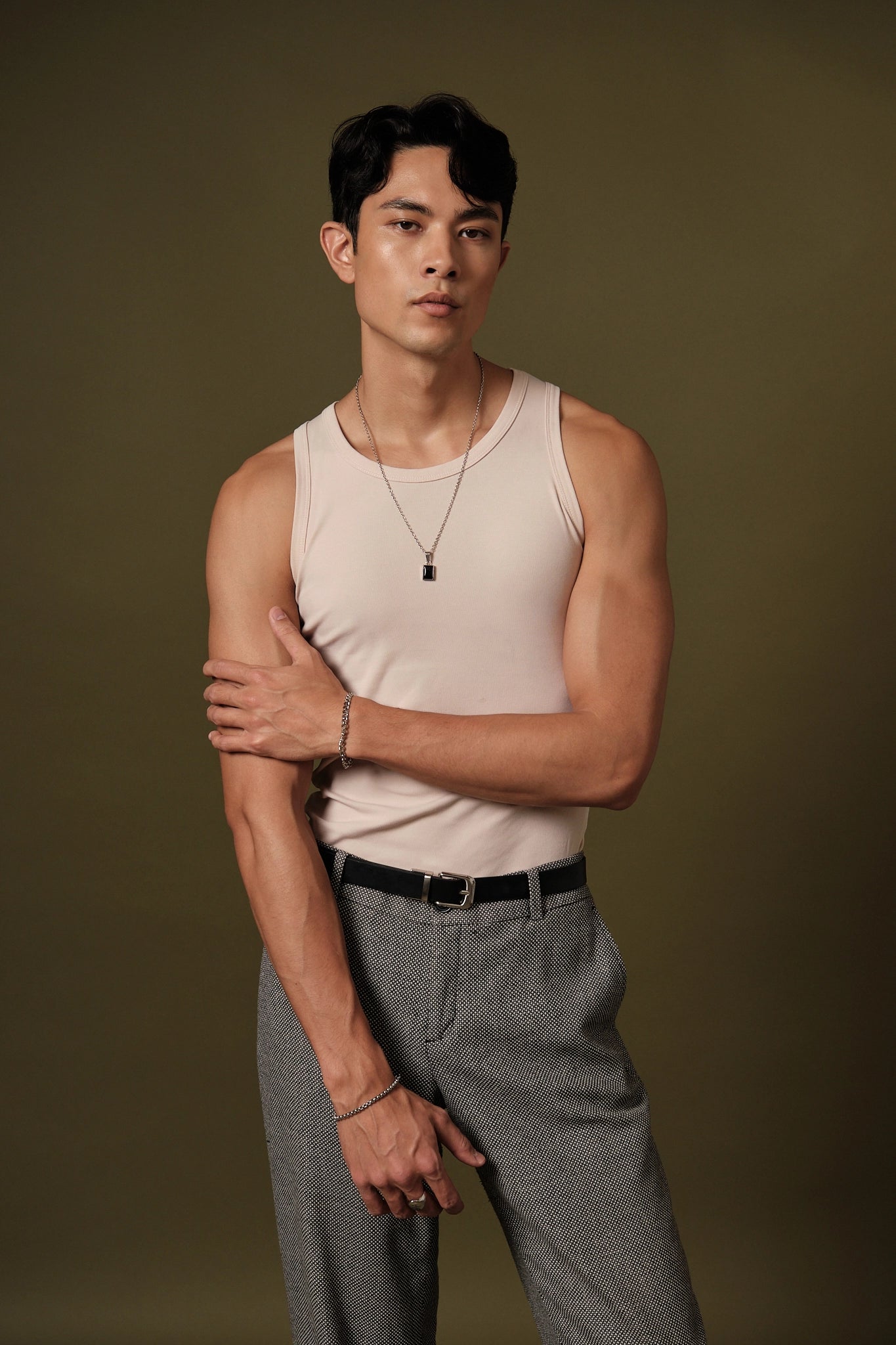 Man wearing a beige tank top and gray pants against a brown background