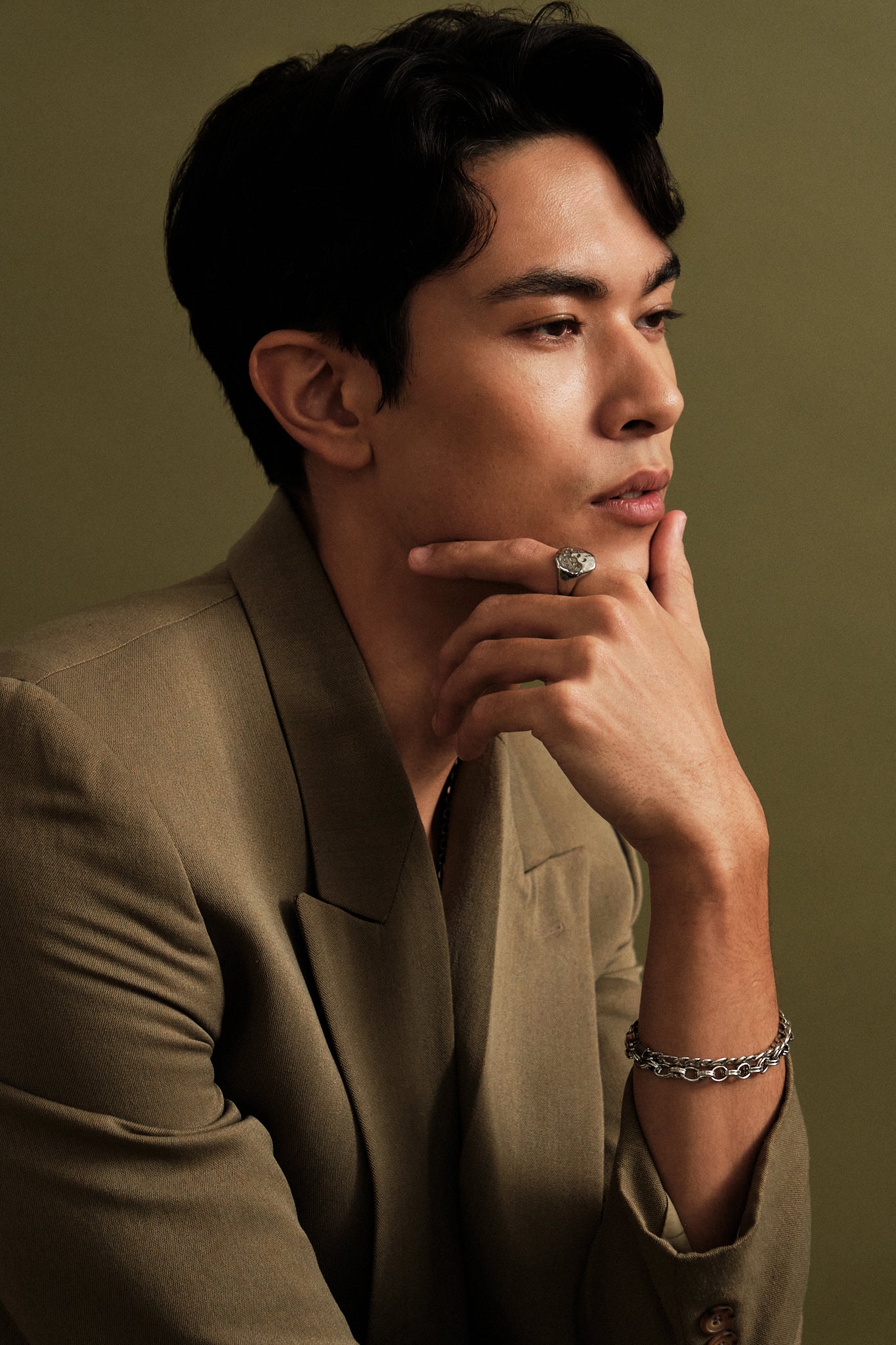 Man in a brown suit with hand on chin against a green background