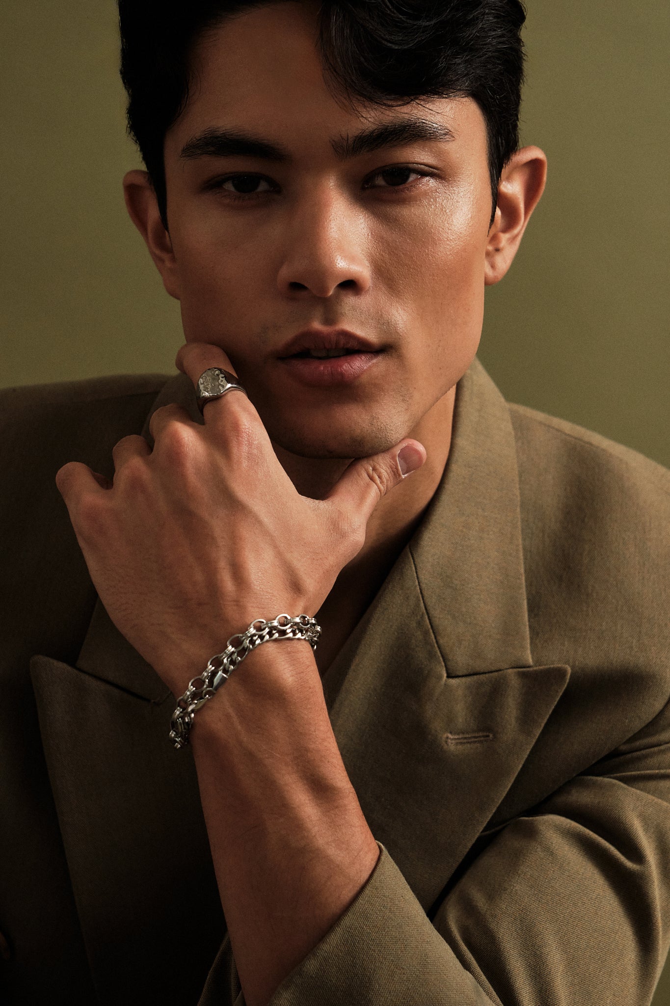 Man wearing a brown coat with a ring and bracelet on a green background