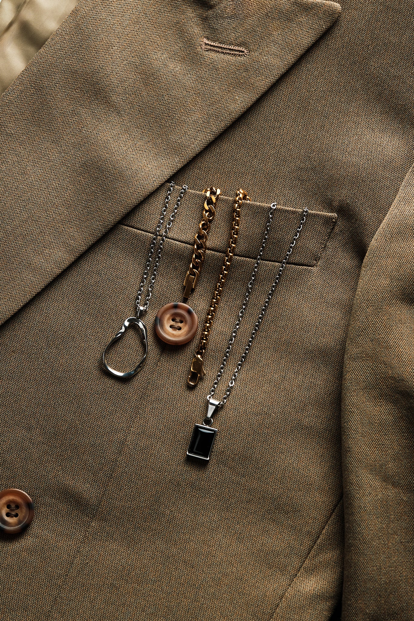 Three necklaces draped over a brown jacket pocket.